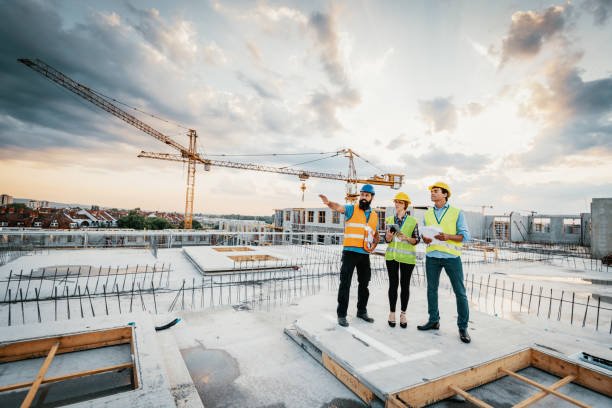 Employees working on construction site, wearing protective equipment and discussing next construction phase - full length models visible on the image